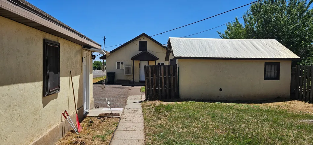 Rear yard featuring a manicured lawn, concrete pathway, and a detached structure with a corrugated metal roof