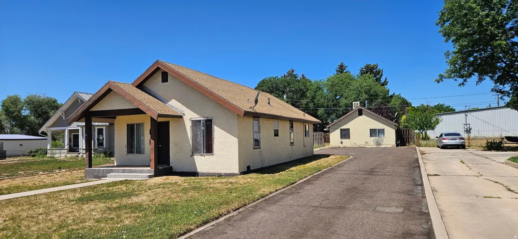 Main home, stucco home with a covered front porch, asphalt shingle roof, and a gravel driveway