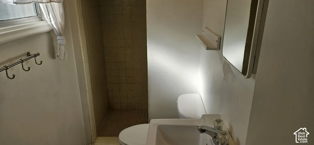 Bathroom featuring a stall shower with tiled surround, wall-mounted sink with dual-handle faucet, integrated medicine cabinet, and wall-mounted shelving