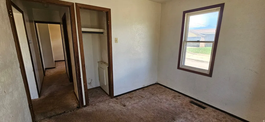 Room featuring a single-pane window with wood-finish trim, a recessed closet with shelving and hanging rod, and textured walls