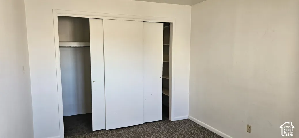 Neutral-toned room featuring patterned carpet flooring, white walls, and a closet with sliding panel doors, integrated shelving, and a built-in clothing rod