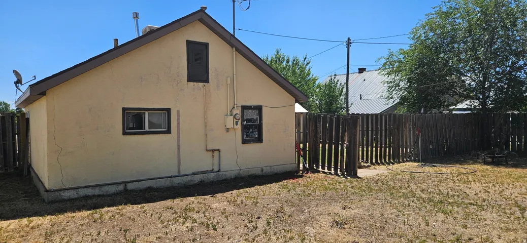 Rear exterior featuring stucco siding, a gabled roofline, and a wood fence