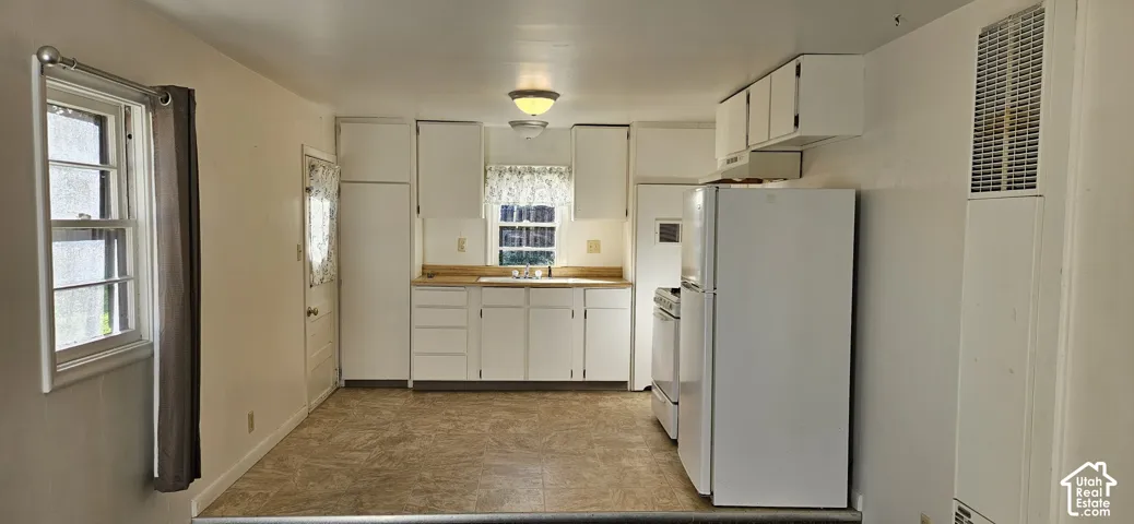 Kitchen featuring white cabinetry, a dual-basin sink, laminate flooring, a white range, and a full-size white refrigerator