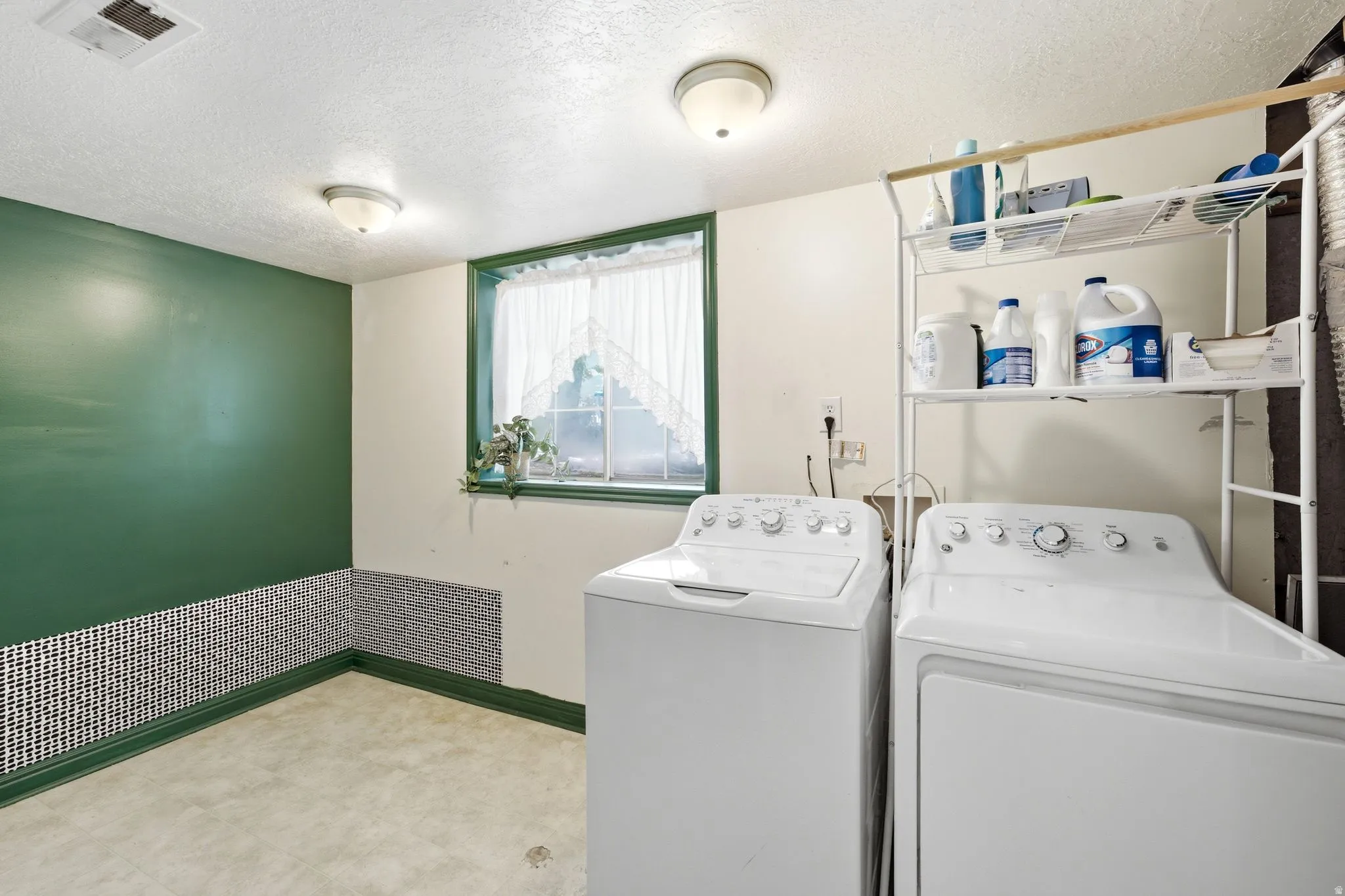 Dedicated laundry area featuring a window with green trim, mosaic tile wainscoting, and a neutral flooring surface