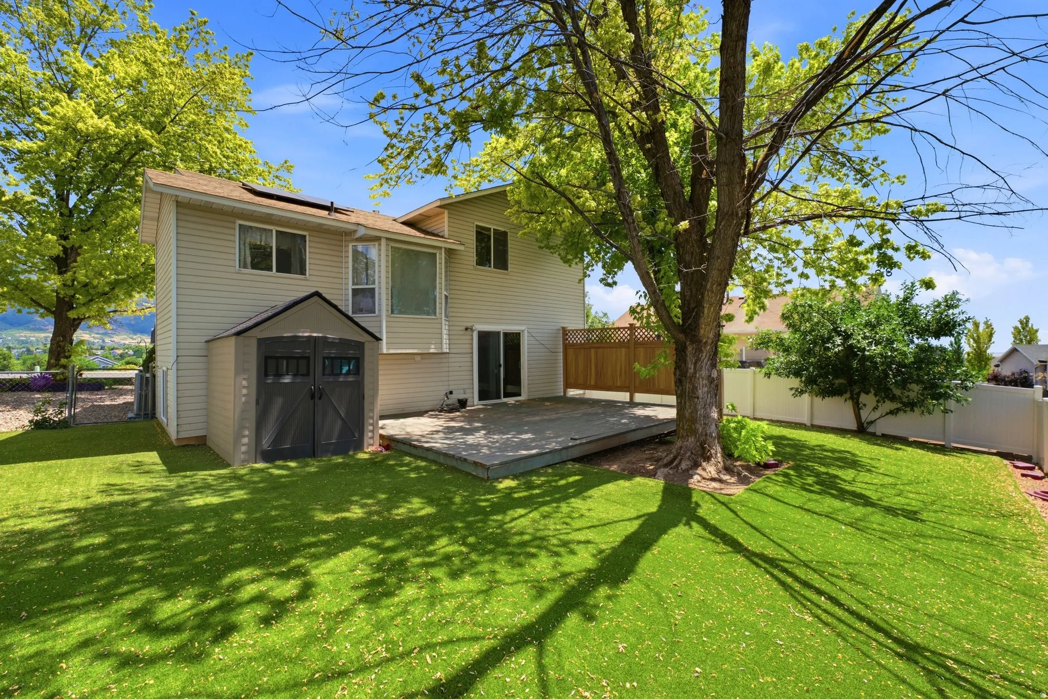 Expansive backyard featuring a large wooden deck, mature shade tree, manicured lawn, and a storage shed
