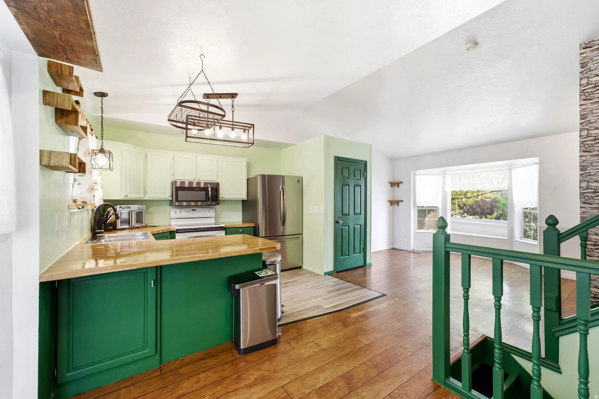 Vaulted ceiling open-concept kitchen featuring light-toned upper cabinetry, green lower cabinetry, and wood-finish countertops