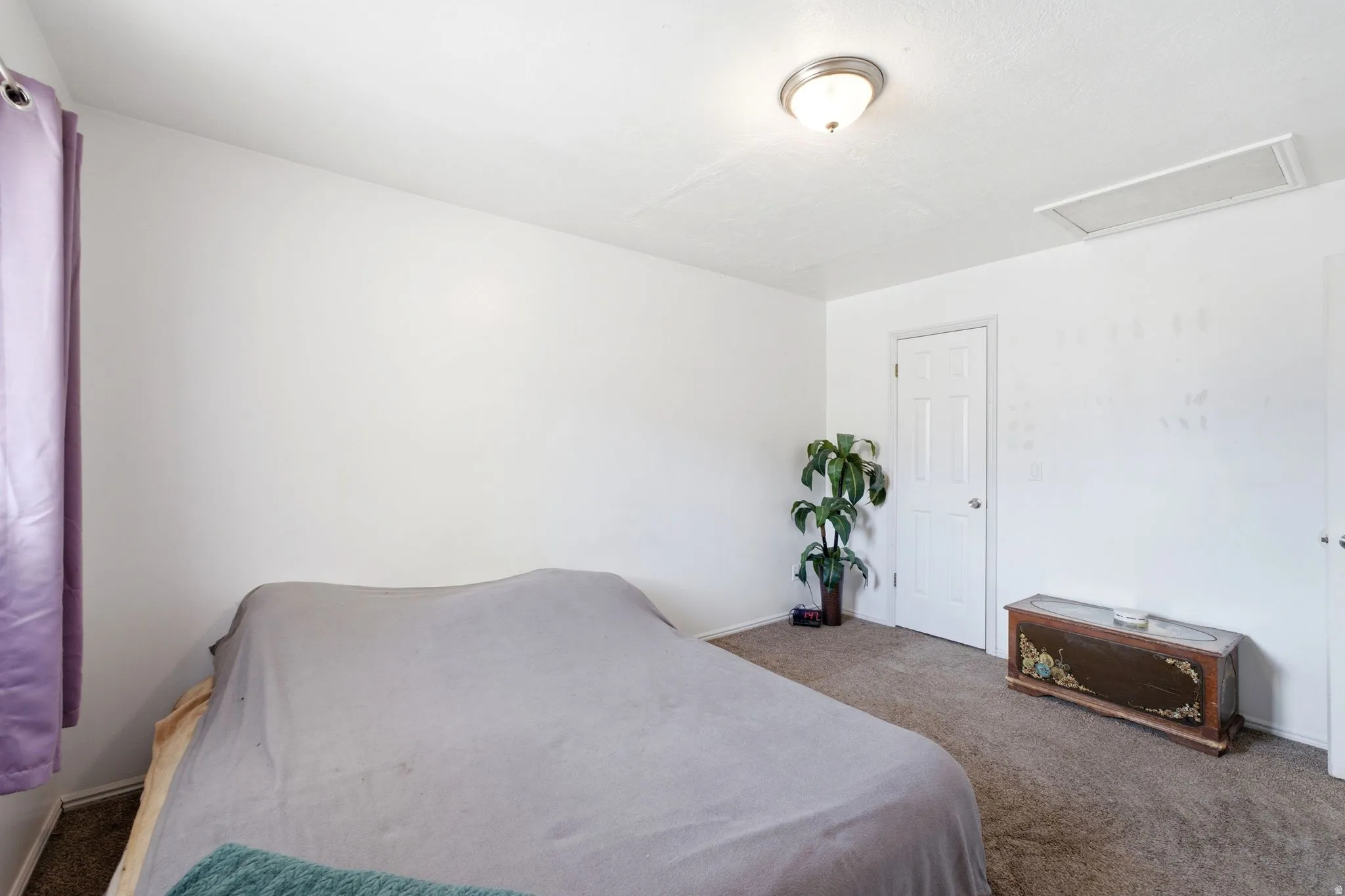 Carpeted room with a ceiling-mounted light fixture, white interior door, and a rectangular ceiling vent