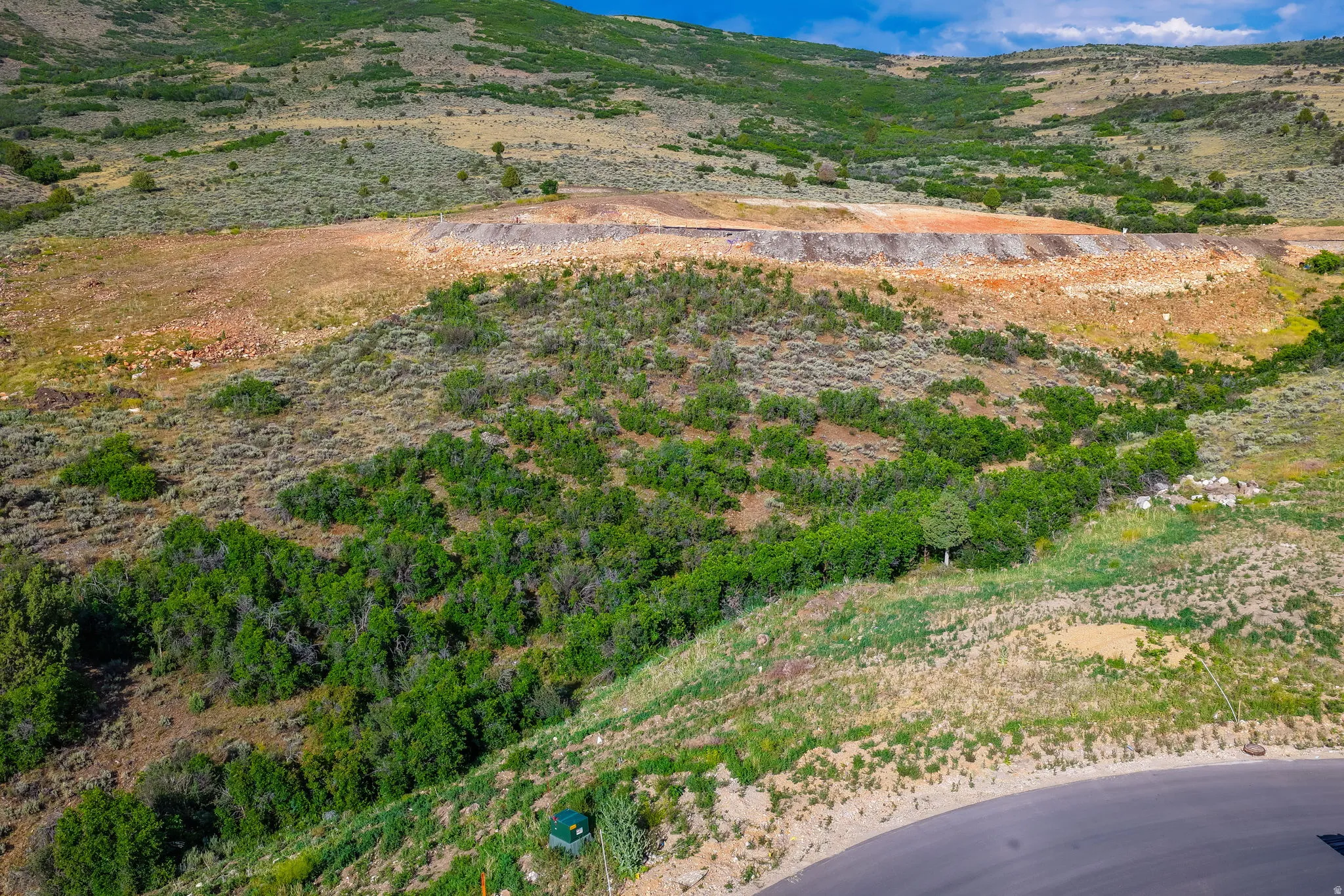 Undulating terrain featuring varied vegetation, natural rock formations, and paved road access