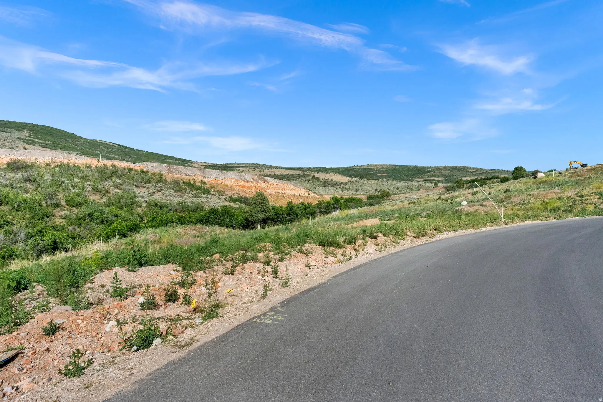Paved road bordering an expansive, undeveloped hillside with varying terrain and natural vegetation under a clear sky