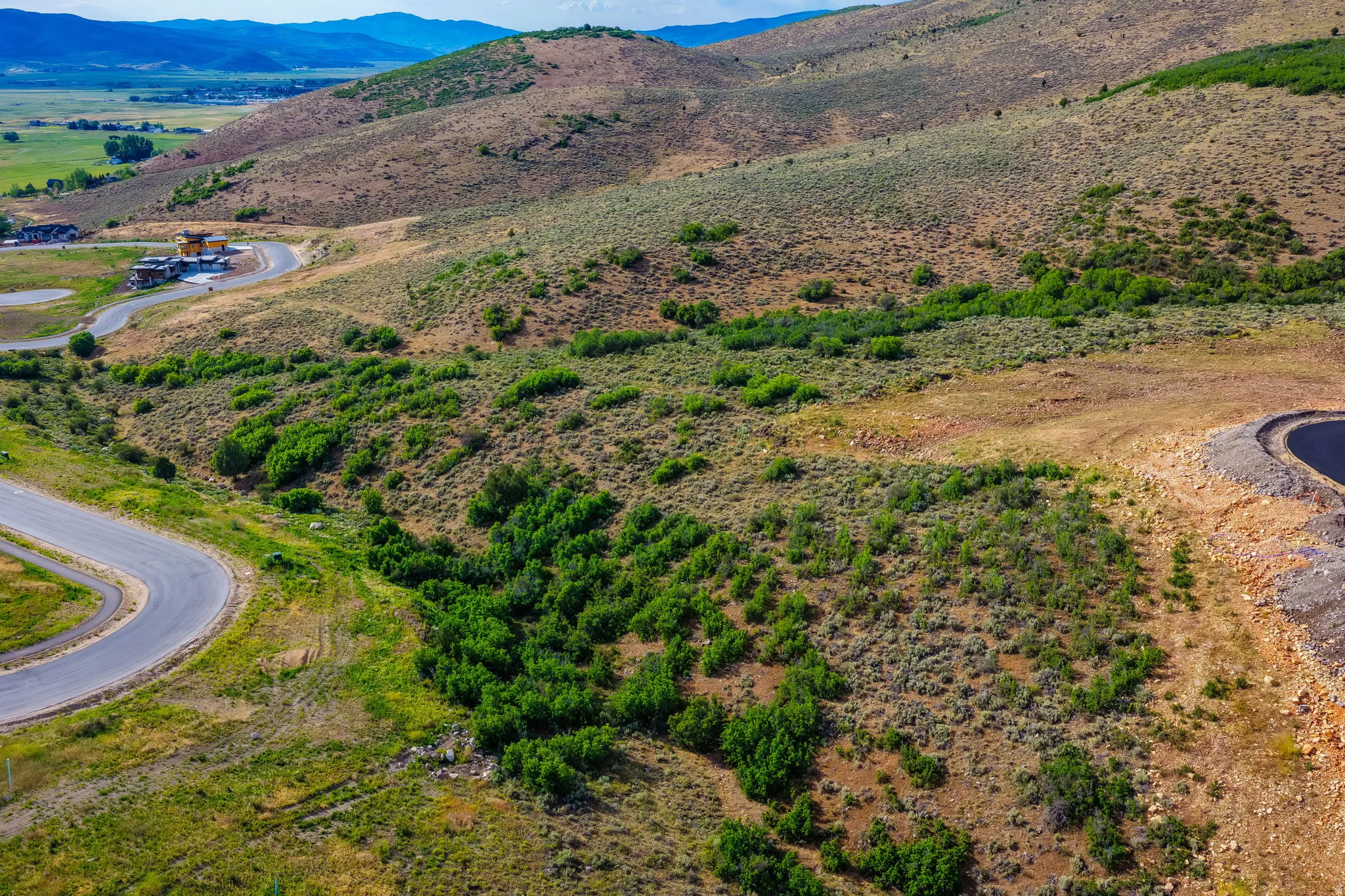 Sloping terrain featuring natural vegetation, winding paved roads, and distant mountain ranges