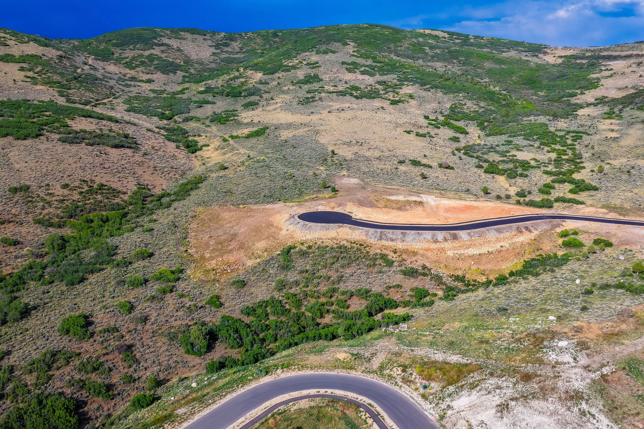 Hillside terrain with natural vegetation, featuring a newly paved asphalt road and a cul-de-sac