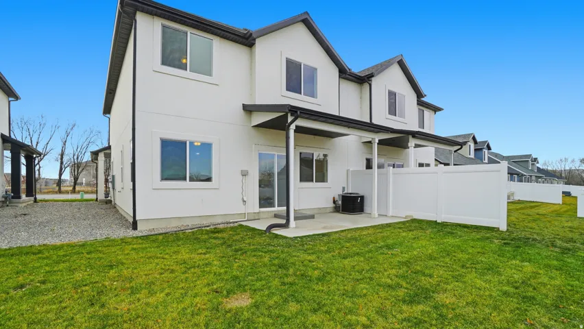 Rear exterior featuring white siding, a covered patio, a sliding glass door, and a private fenced yard with green lawn