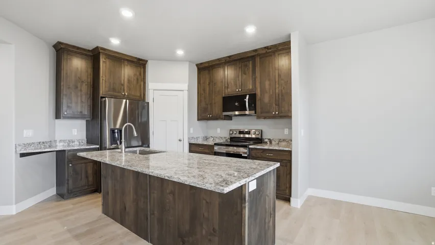 Kitchen featuring a central island with an undermount sink, granite countertops, wood-finish cabinetry, recessed lighting, and light wood-finish flooring
