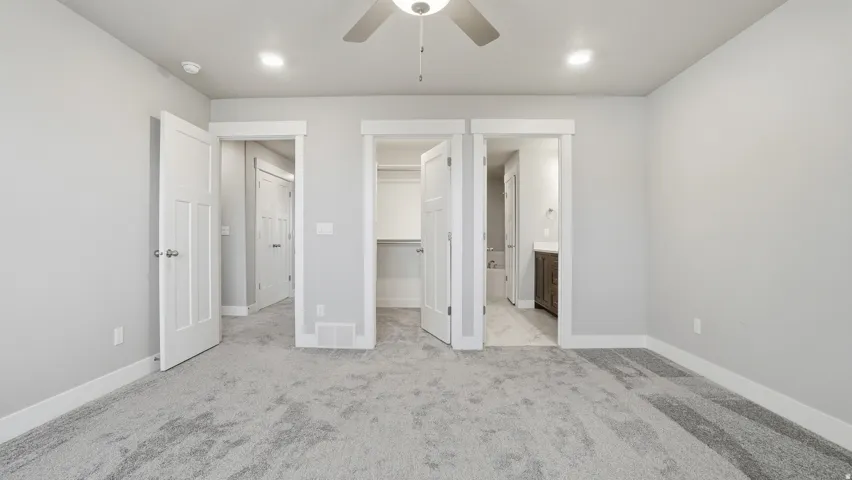 Spacious room featuring light gray walls, plush gray carpeting, white trim, a ceiling fan with integrated lighting, and multiple doorways leading to other areas