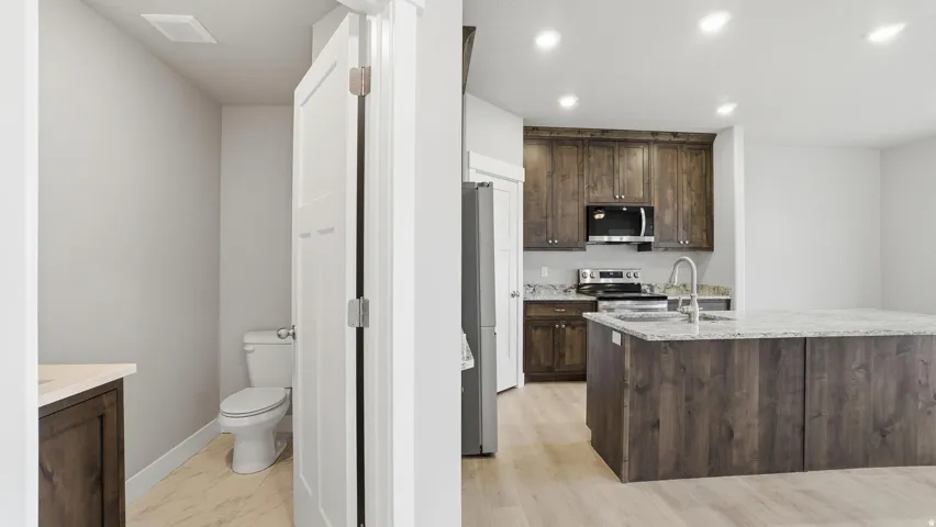 Modern kitchen featuring dark wood cabinetry, stainless steel appliances, and a large central island with a granite-style countertop