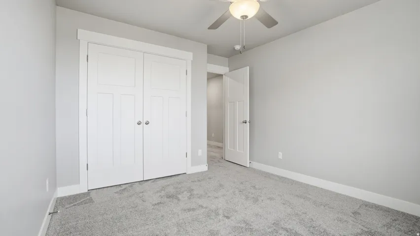 Bedroom featuring light gray walls, gray carpeting, a white bi-fold closet, and a ceiling fan with integrated lighting