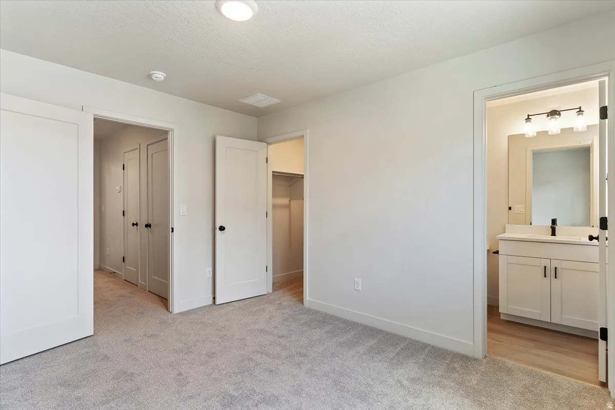 Spacious carpeted room featuring a ceiling-mounted light fixture, white trim, and doors with black hardware