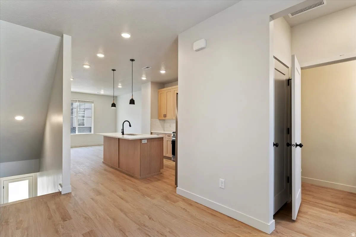 Open-concept living space featuring wood-finish flooring, recessed lighting, and a modern kitchen island with black pendant lights