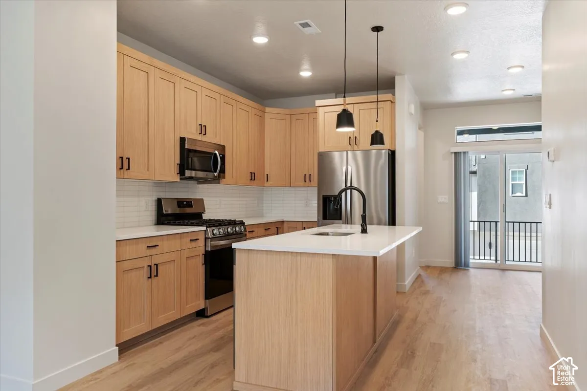 Open-concept kitchen featuring wood-finish cabinetry, stainless steel appliances, white subway tile backsplash, and an island with a matte black faucet