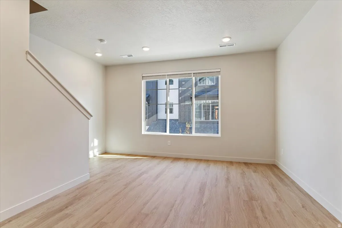 Spacious room featuring light wood-finish flooring, recessed lighting, and a large window with white trim