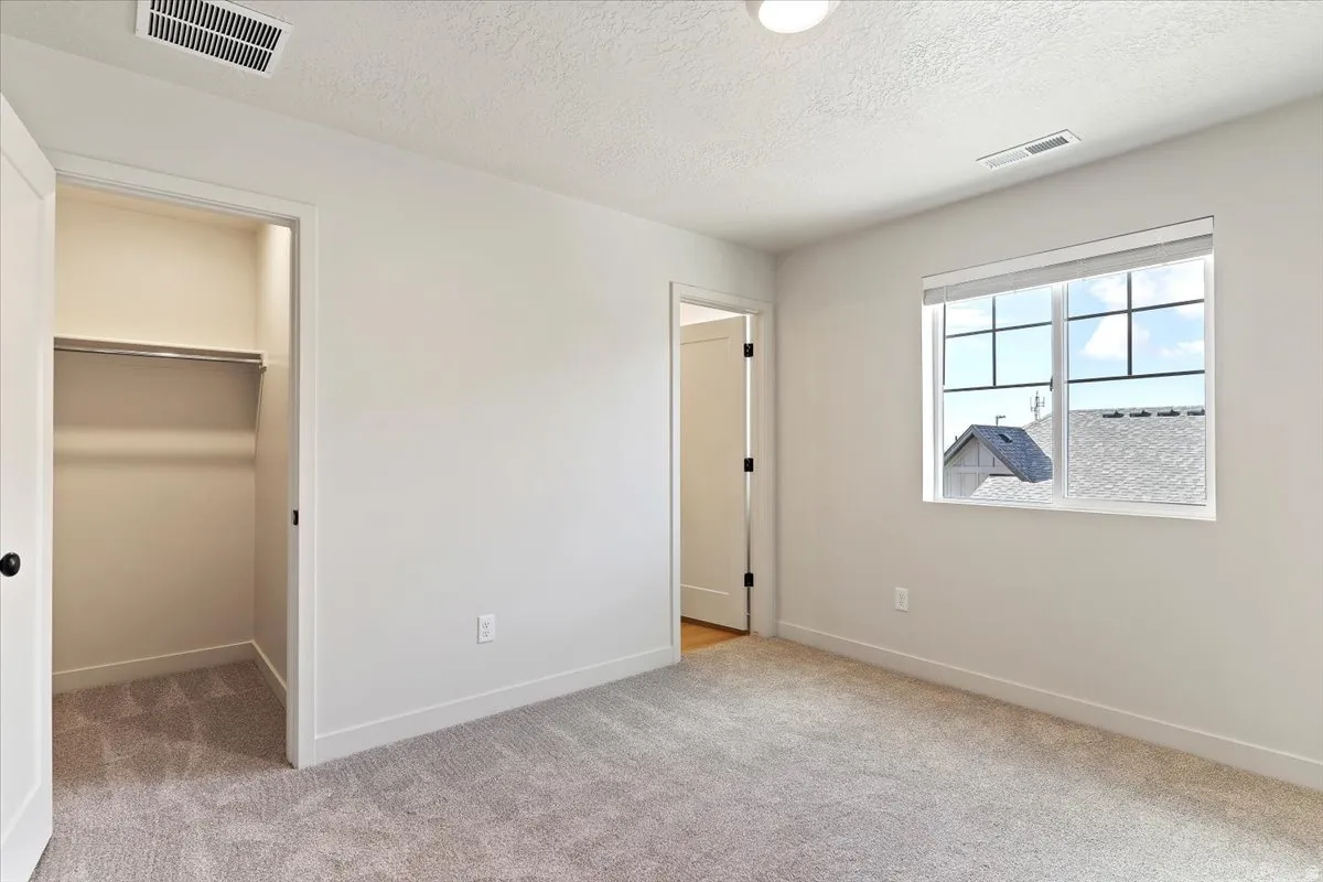 Spacious room featuring neutral carpeting, white walls, a large window, a built-in closet with shelving, and a modern overhead light fixture