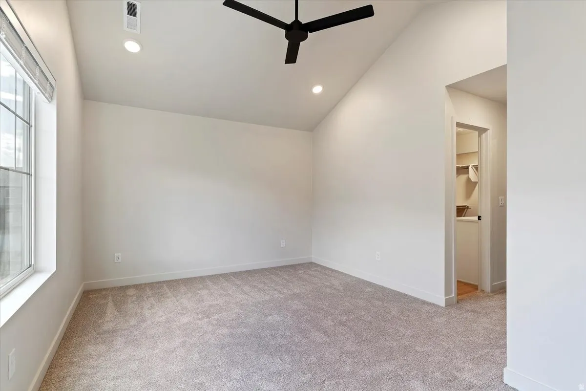 Carpeted room featuring a vaulted ceiling with a black ceiling fan, recessed lighting, and a large window