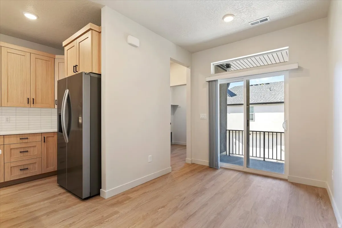 Contemporary kitchen and dining area featuring wood-finish flooring, light-toned cabinetry with dark hardware, and a stainless steel refrigerator