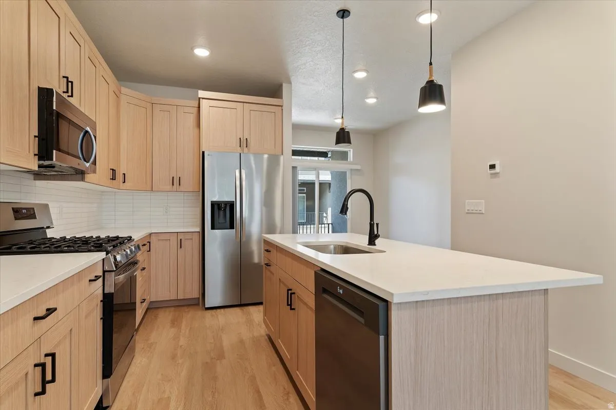 Contemporary kitchen featuring light wood-finish cabinetry, stainless steel appliances, a white subway tile backsplash, and a central island with a white countertop