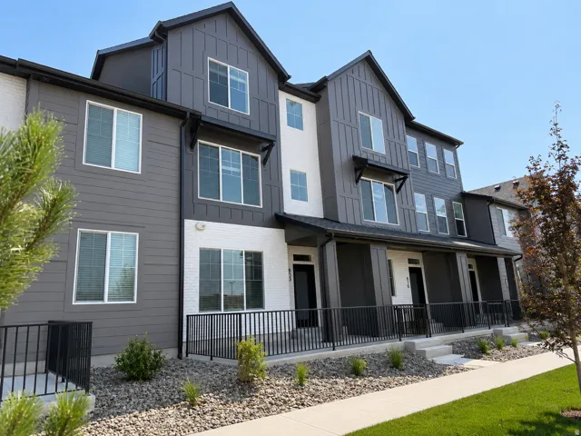 Modern townhome exterior showcasing a multi-level design, a blend of gray horizontal siding and white brick accents, vertical board and batten detailing, multiple windows, and a covered porch with black metal railings
