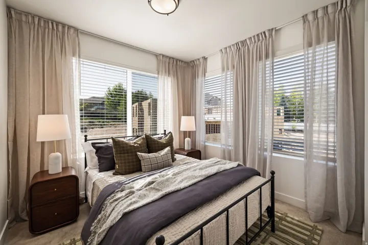 Bedroom featuring a wall of multiple windows with horizontal blinds and floor-length drapery