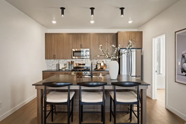 Kitchen featuring a central island with seating for three, stainless steel appliances, wood-finish cabinetry, a patterned tile backsplash, and overhead track lighting