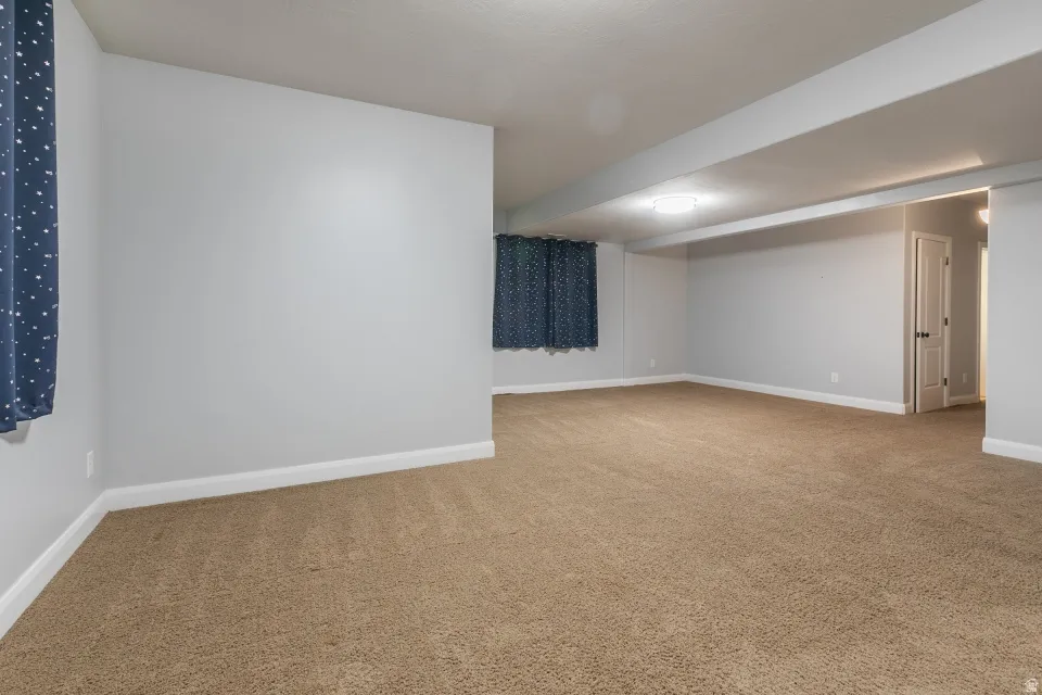Spacious carpeted room featuring light gray walls, white trim, recessed lighting, and a white interior door