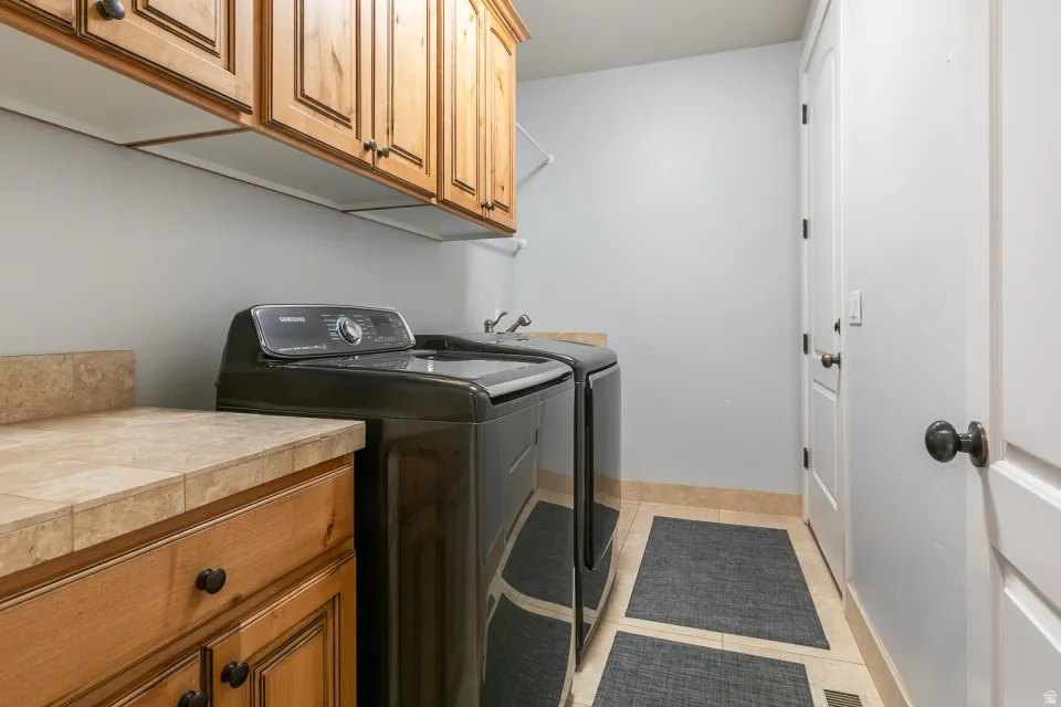 Laundry area featuring wood cabinetry, tiled countertops, and light tile flooring