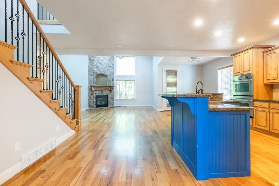 Open-concept layout featuring wood-finish flooring, a stone-clad fireplace, and a striking blue kitchen island with a granite-style countertop