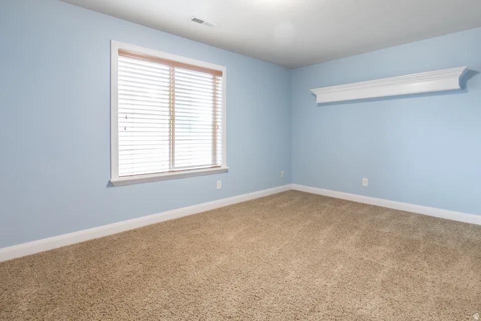 Carpeted room featuring a window with blinds, white trim, a decorative wall shelf, and light blue walls