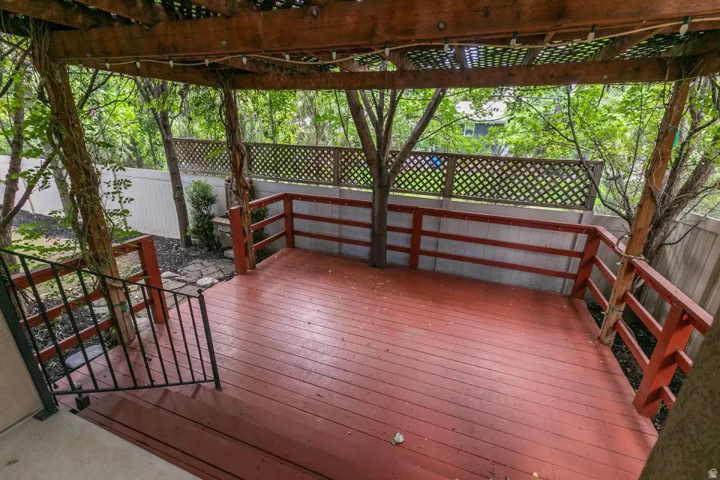 Spacious outdoor deck with reddish-brown flooring, featuring a slatted wood pergola, integrated trees, and a latticework fence