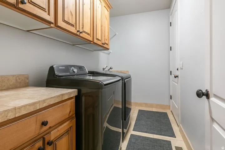 Laundry area featuring wood cabinetry, tiled countertops, and light tile flooring