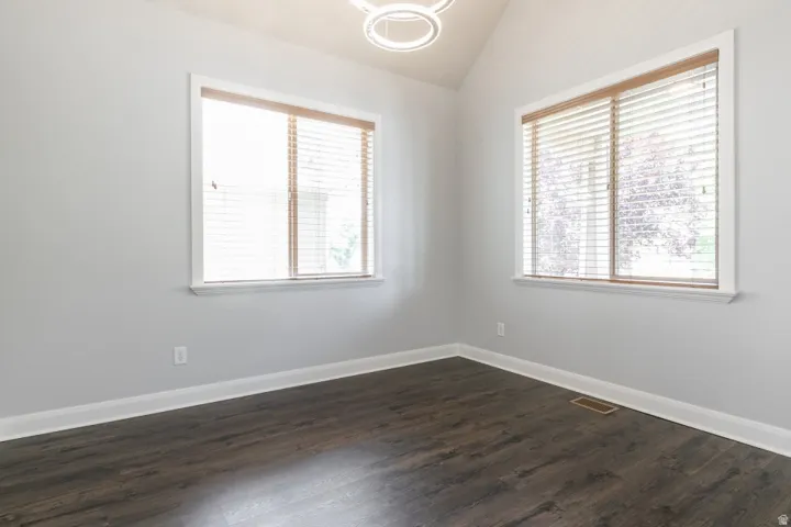 Vaulted ceiling featuring a contemporary circular light fixture, wood-finish flooring, and two windows with blinds