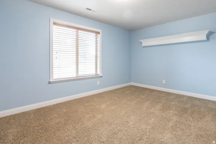 Carpeted room featuring a window with blinds, white trim, a decorative wall shelf, and light blue walls