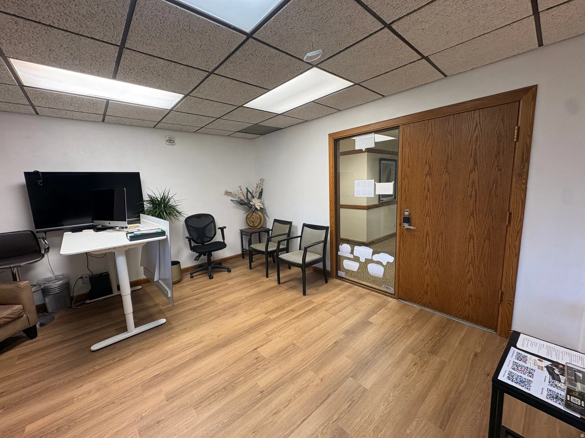 Office space featuring wood-finish flooring, white walls, and a suspended acoustic ceiling with integrated fluorescent lighting