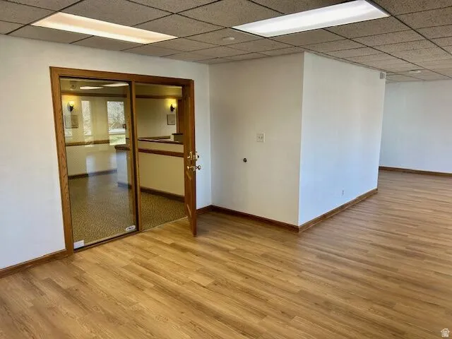 Interior space featuring wood-finish flooring, white walls, and a suspended acoustic tile ceiling with fluorescent lighting