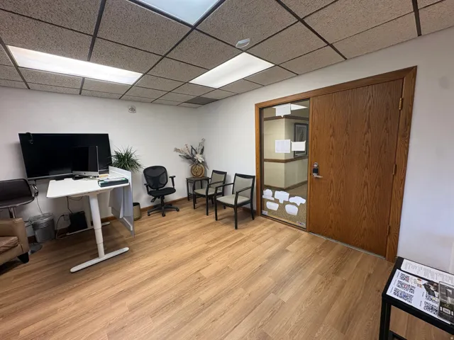 Office space featuring wood-finish flooring, white walls, and a suspended acoustic ceiling with integrated fluorescent lighting