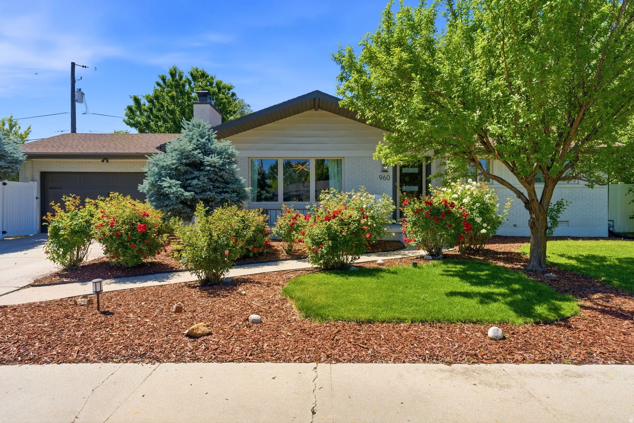 Front exterior featuring a dark garage door, white privacy fence, and a stone chimneyhttps://www.utahrealestate.com/lip/photo/listno/2170555#
