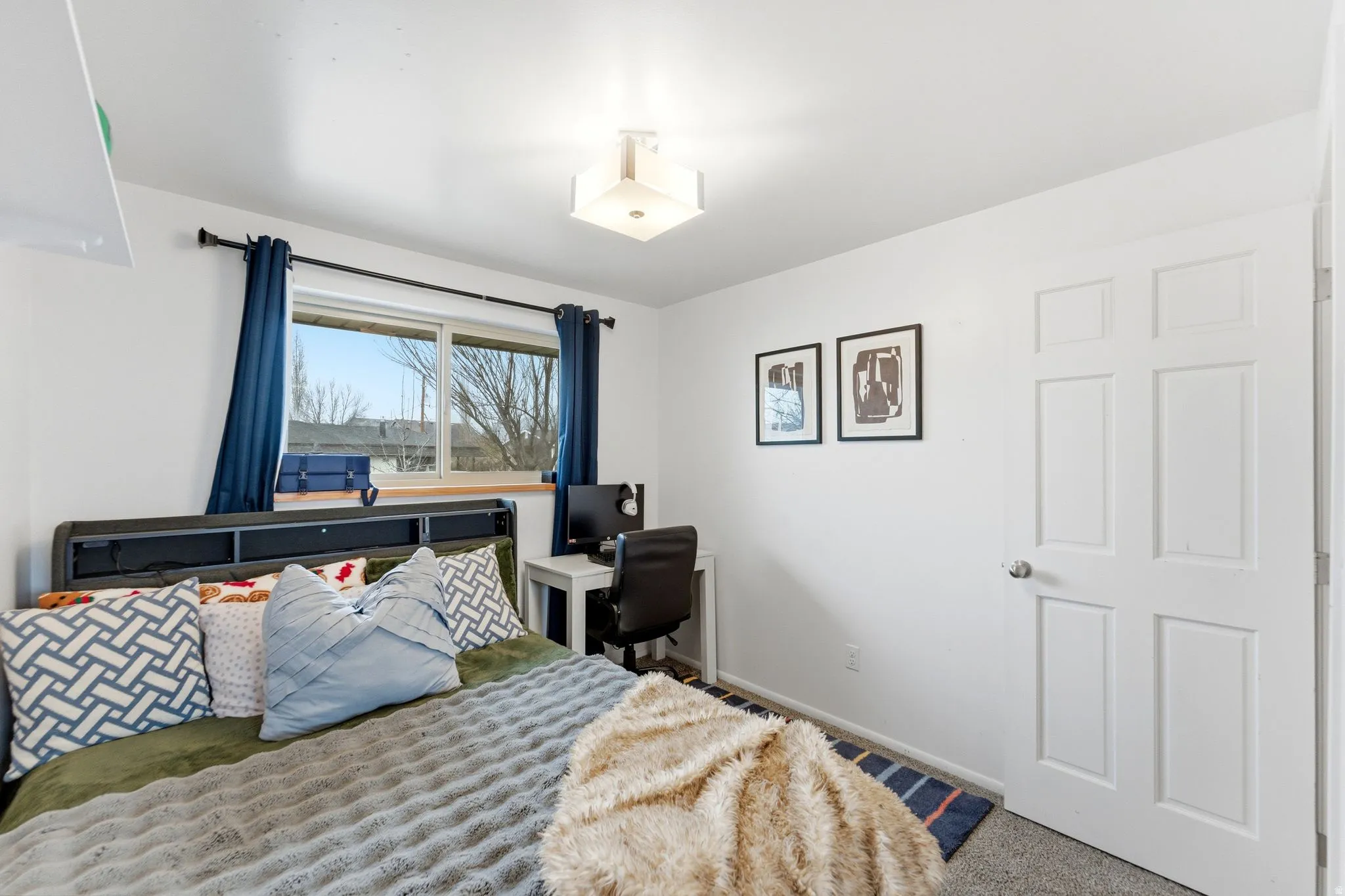 Bedroom featuring a window with blue drapes, light gray carpet flooring, white walls, and a white six-panel door