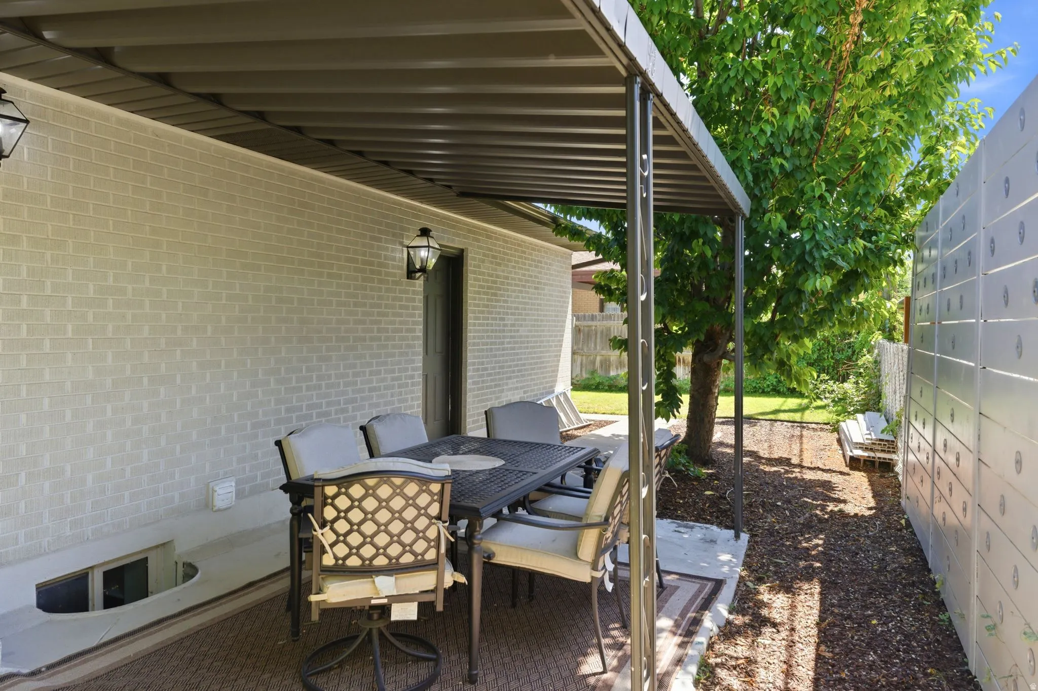 Covered patio featuring a solid roof structure, light-colored brick exterior, and a built-in window well