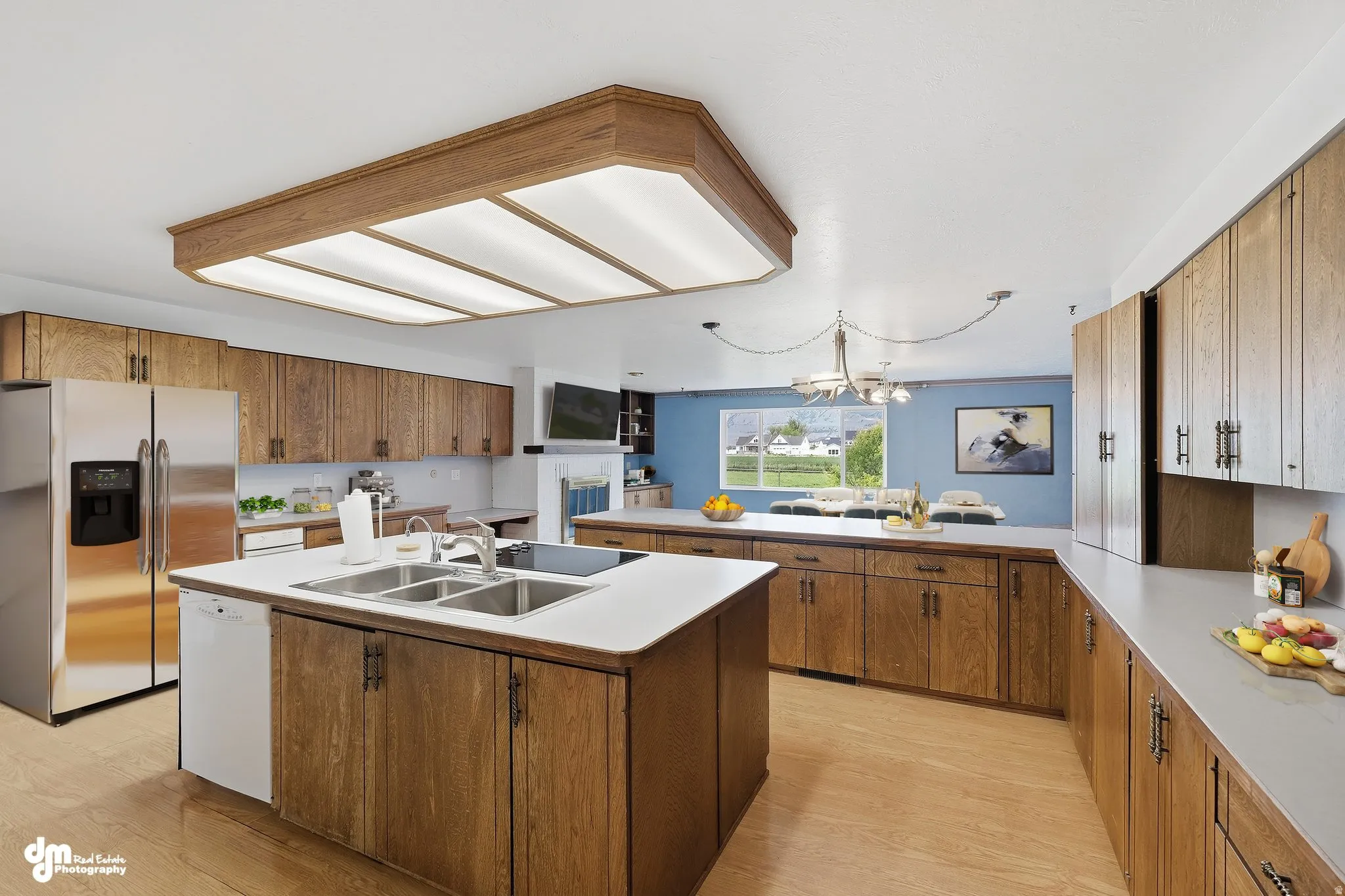 Galley kitchen featuring wood-finish cabinetry, stainless steel appliances, a center island with a double basin sink, and ample countertop space