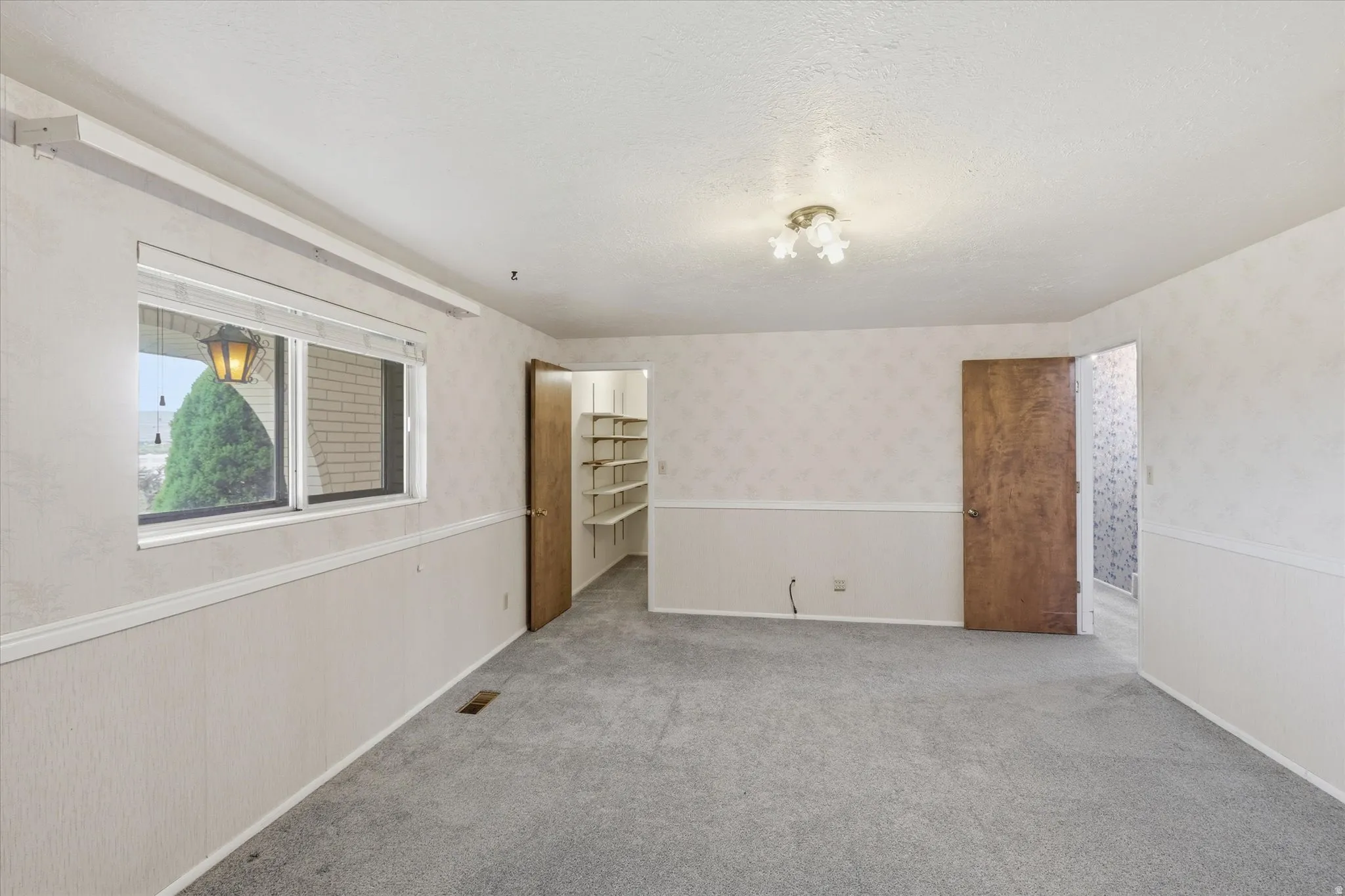 Interior room featuring light gray carpeting, wainscoting, and patterned wallpaper