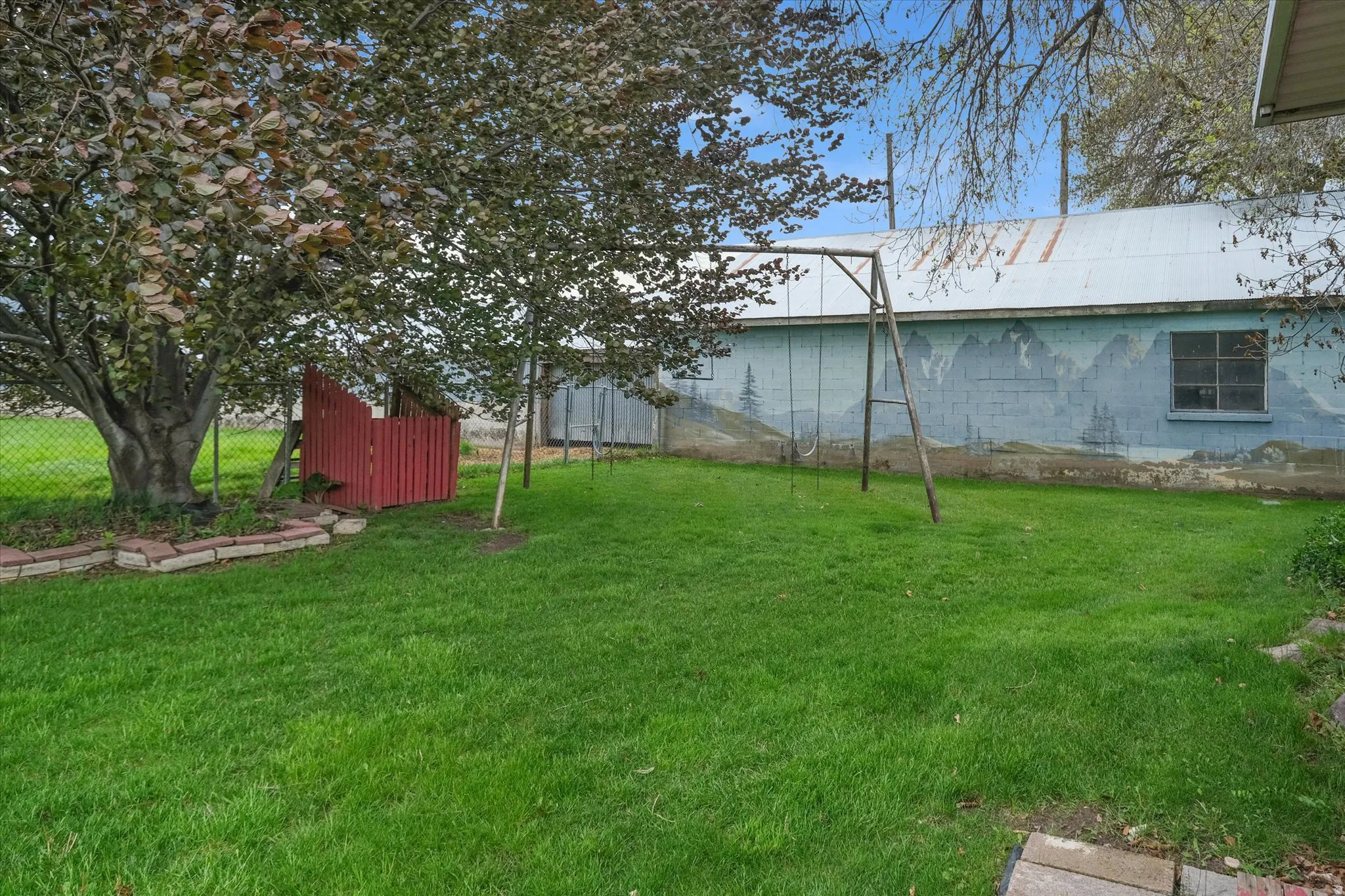 Green lawn with mature trees and a chain link fence