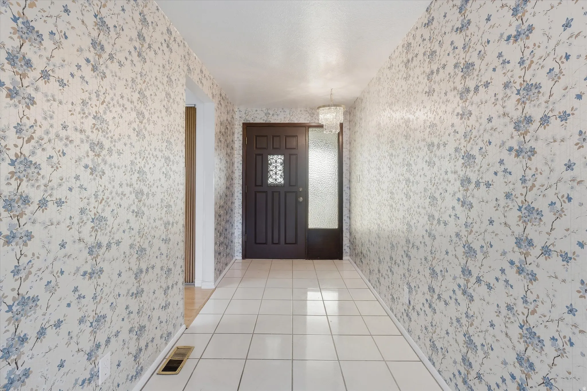 Entryway featuring a dark wood-finish door with decorative glass, a frosted glass sidelight, tile flooring, and floral pattern wallpaper