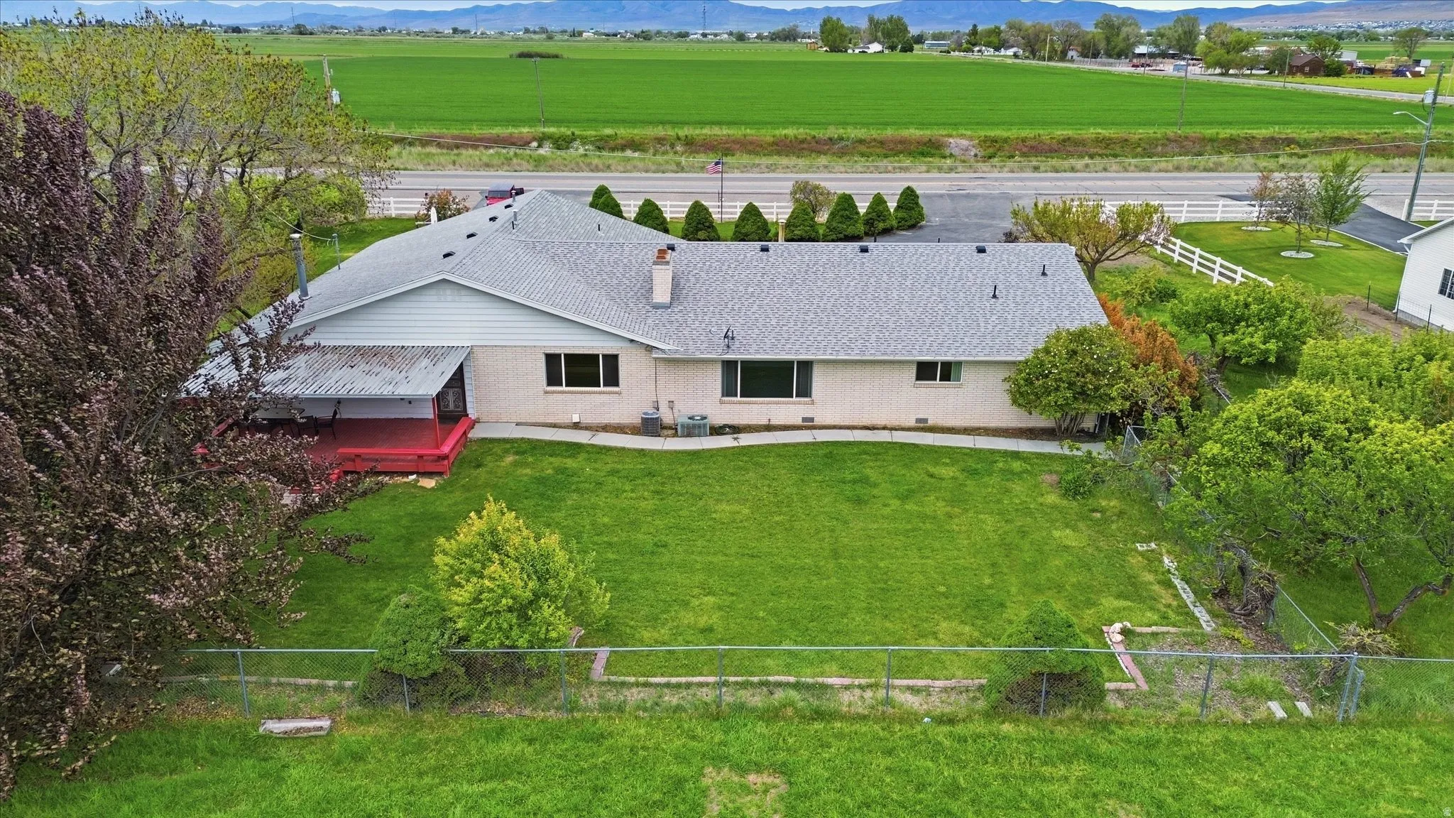Green lawn with established landscaping, perimeter fencing, and mature trees